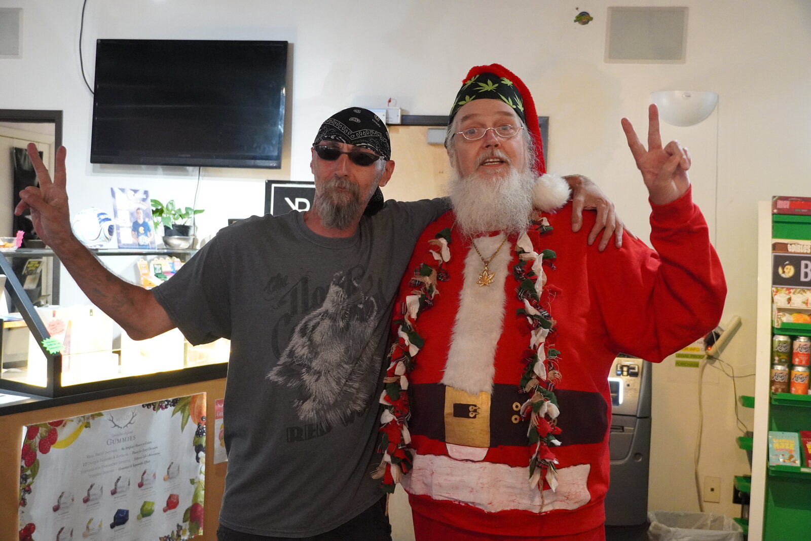 Smoking Santa and a customer flashing peace signs beside a WYLD gummies display