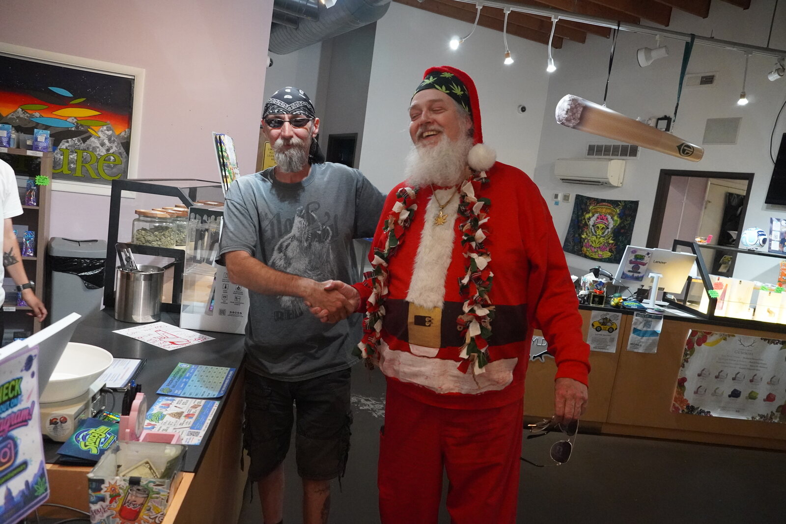 Smoking Santa shaking hands with a customer across a dispensary counter